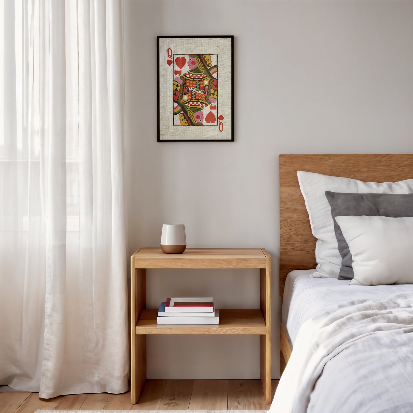 A framed art print of a Queen of Hearts playing card hangs on a light gray wall above a wooden nightstand in a modern bedroom setting.