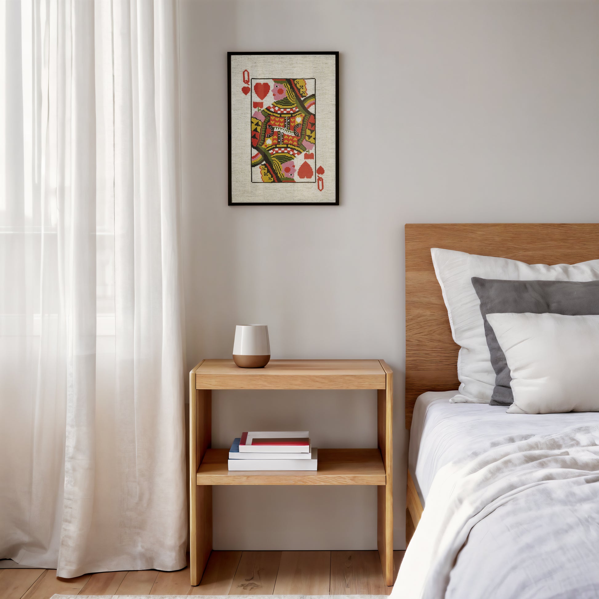 A framed art print of a Queen of Hearts playing card hangs on a light gray wall above a wooden nightstand in a modern bedroom setting.