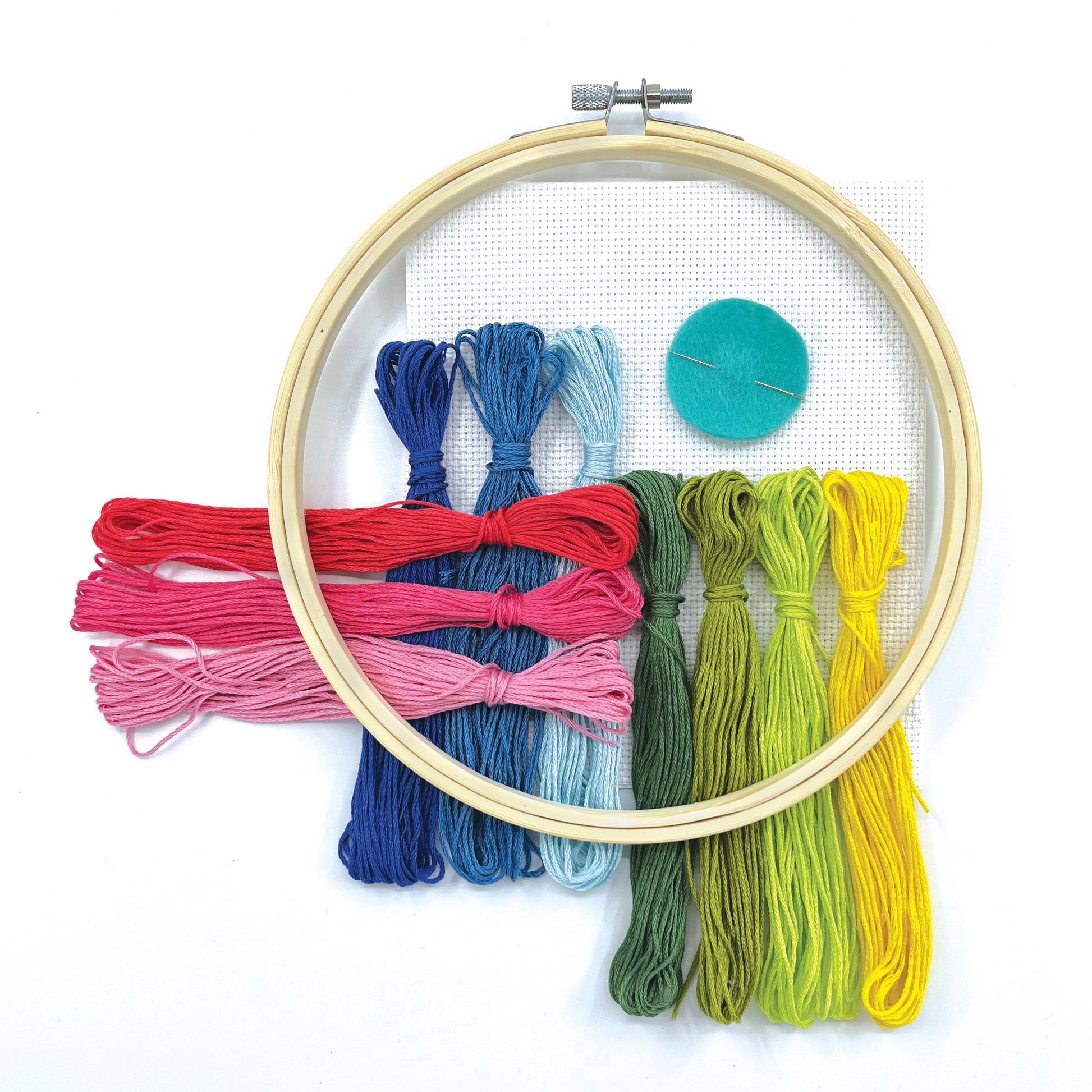 A wooden embroidery hoop with a metal tension clamp, holding a white mesh panel over a set of colorful embroidery floss threads in blue, pink, green, yellow, and teal, arranged on a plain white background.